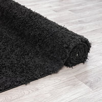 Rolled black modern shaggy runner rug with thick plush polyester fibers on light wood floor.