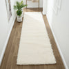 Cream shaggy runner rug with thick plush pile on wooden floor in bright hallway.