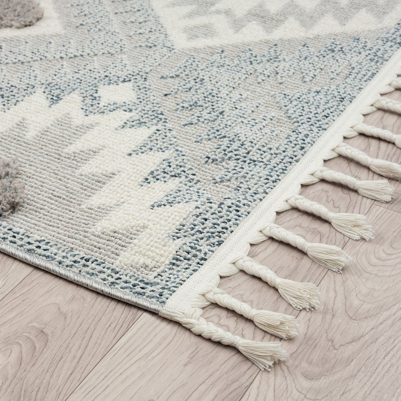 Grey and cream geometric patterned runner rug with textured pile and fringed edges on light wood floor.