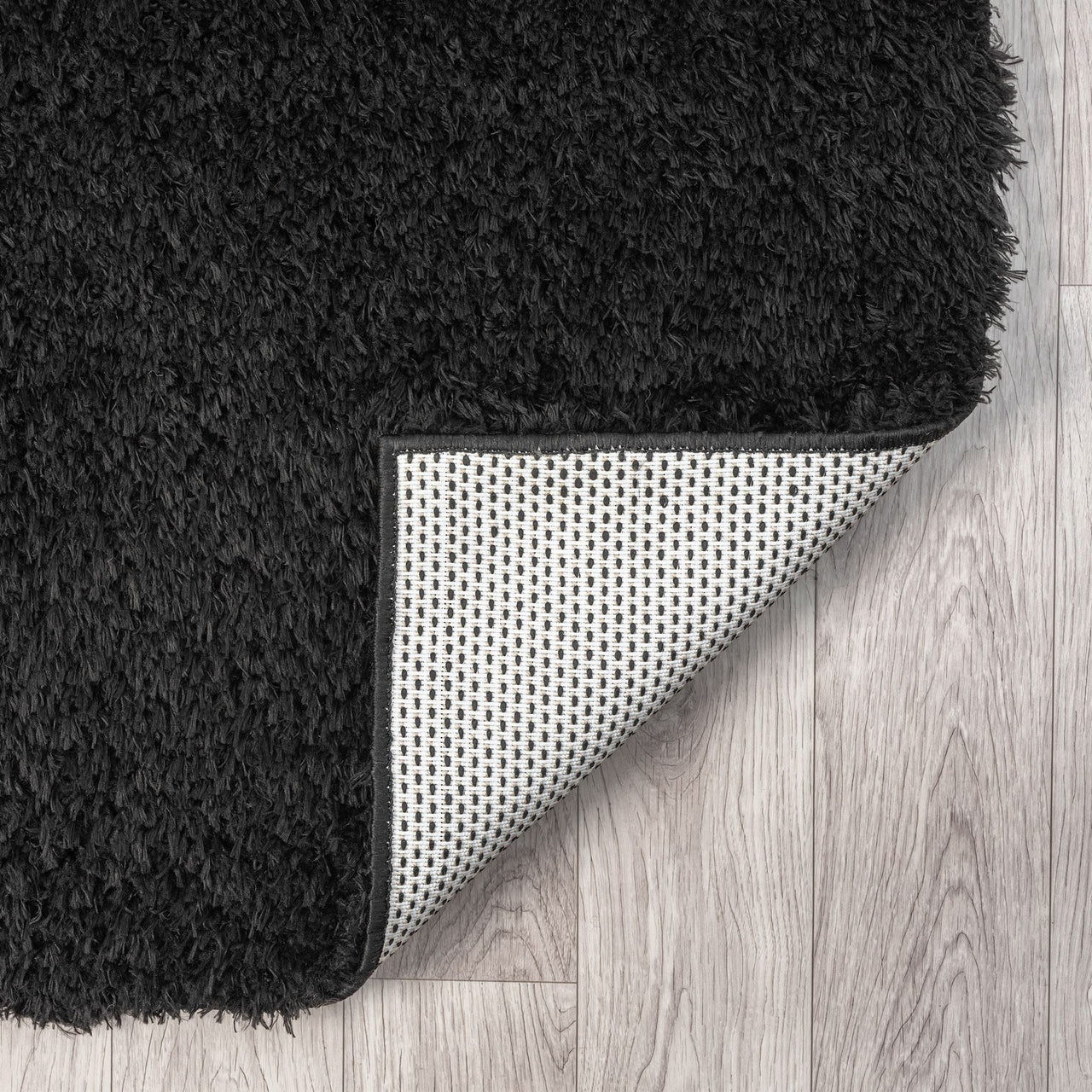 Black modern shaggy runner rug with dense polyester fibers and anti-slip backing on light wood floor.