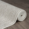 Beige flatweave rug with subtle geometric pattern and tightly woven texture rolled on dark wood floor.