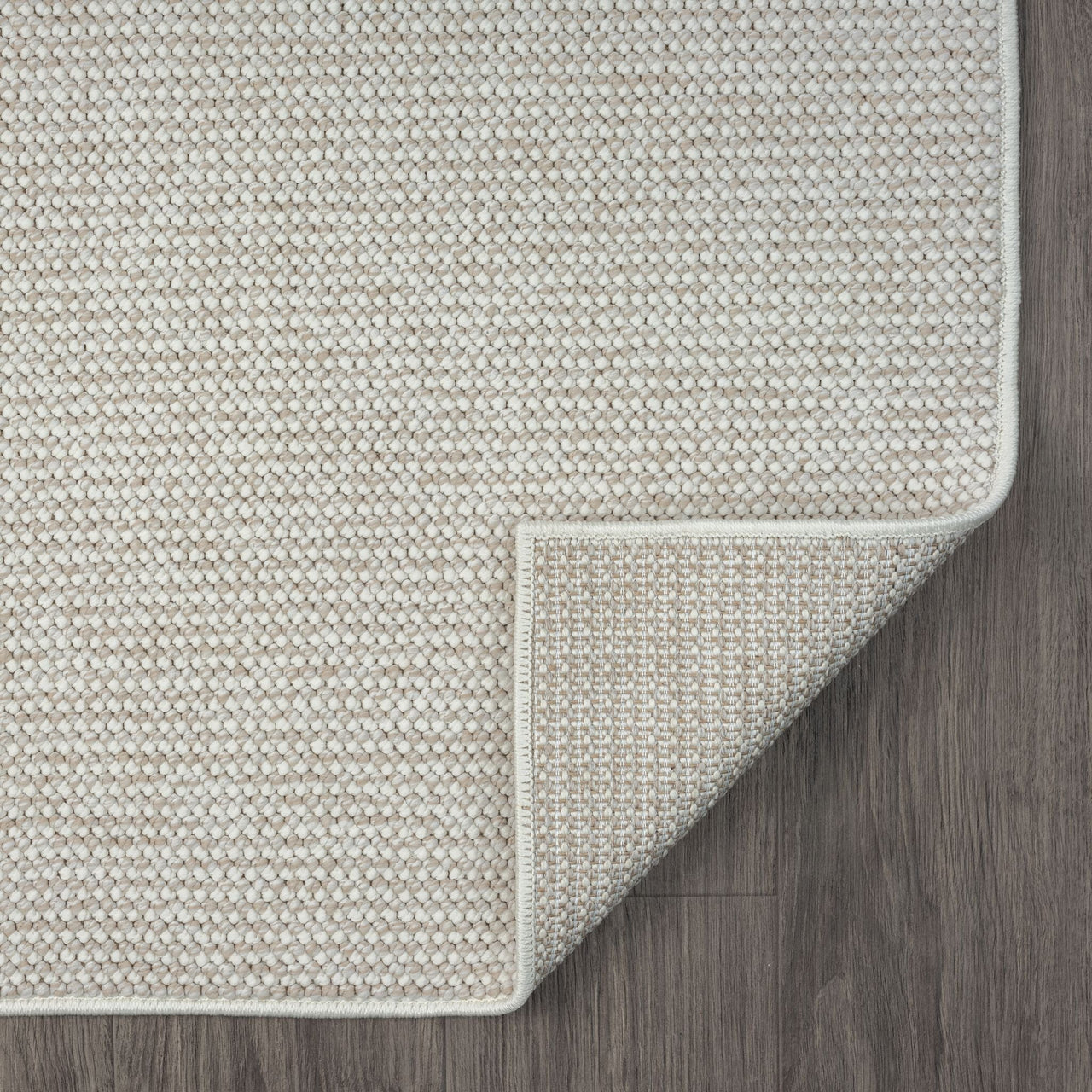 Beige flatweave rug with subtle geometric texture and piped edges on dark wood floor.