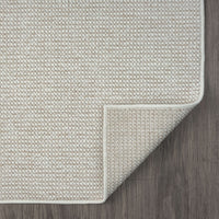 Beige flatweave rug with subtle geometric texture and piped edges on dark wood floor.