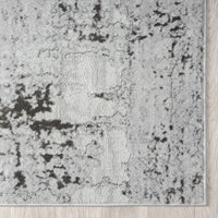 Close-up of a textured gray and black area rug on a wooden floor.