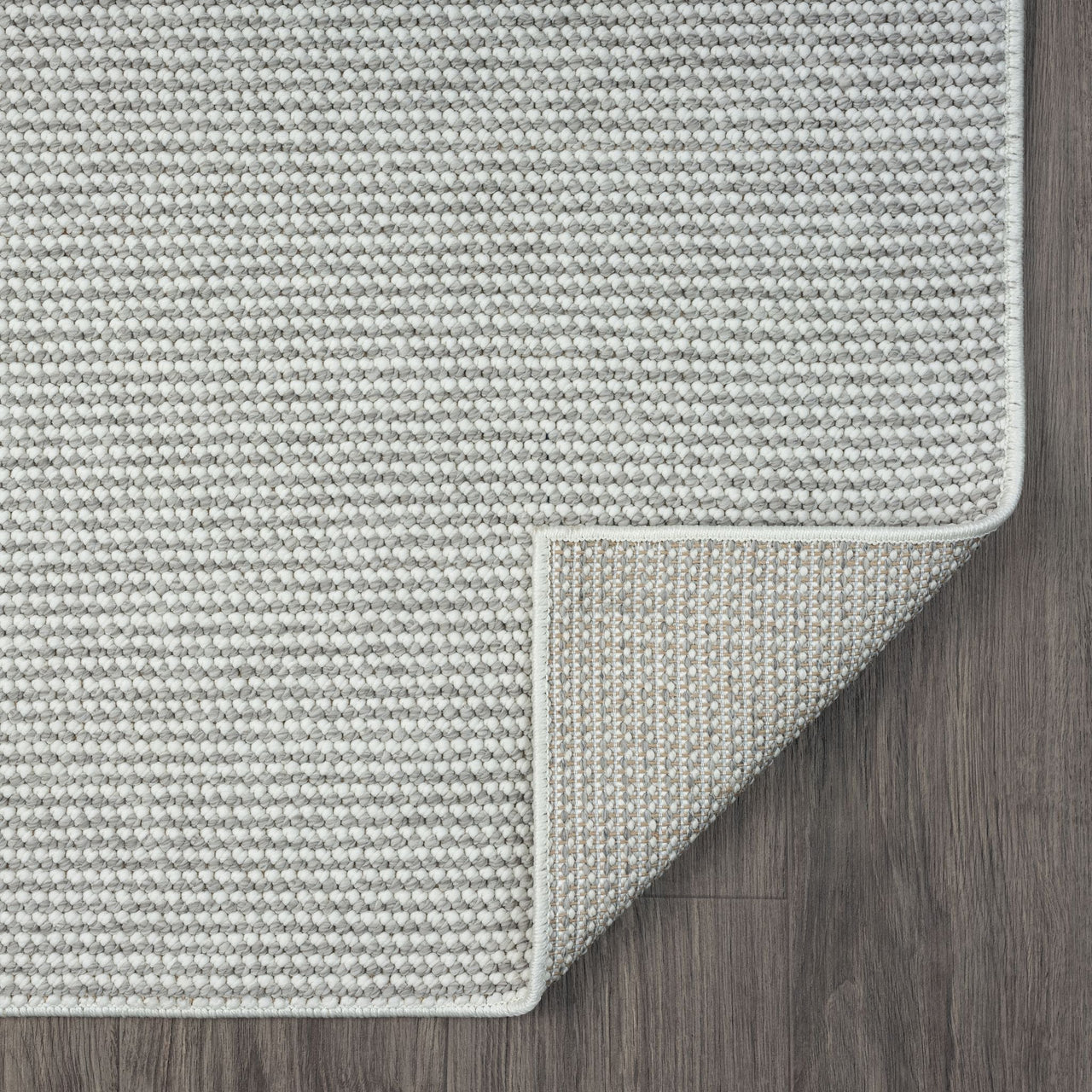Silver grey flatweave rug with subtle geometric texture and clean, finished edges on dark wood floor.