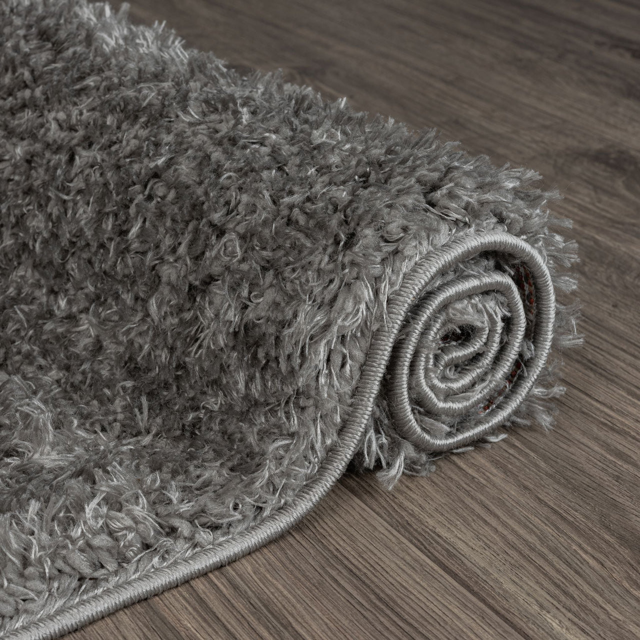 Rolled grey and silver modern shaggy runner rug with thick plush texture on dark wood floor.