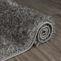 Rolled grey and silver modern shaggy runner rug with thick plush texture on dark wood floor.
