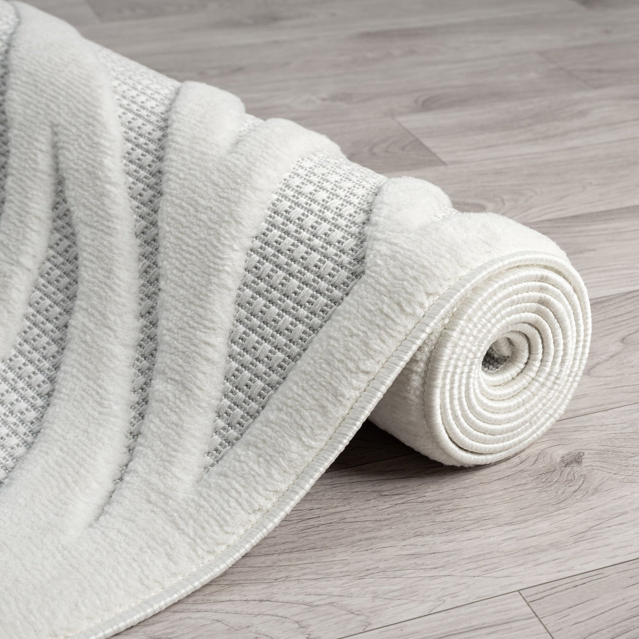 Ivory geometric patterned modern rug with textured polypropylene pile rolled on wooden floor.