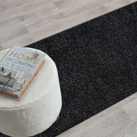 Black modern shaggy runner rug with dense plush pile on light wood floor.