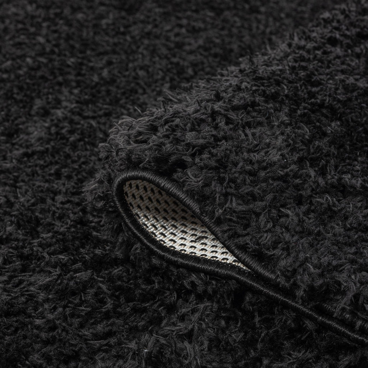 Black modern shaggy rug with thick polyester fibers and a non-slip backing edge visible.