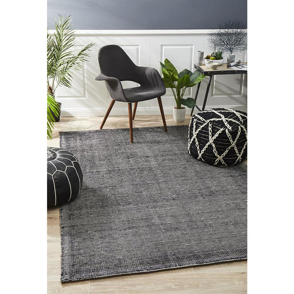 Black modern cut loop pile rayon cotton rug with subtle texture and fringed edges on light wood floor.