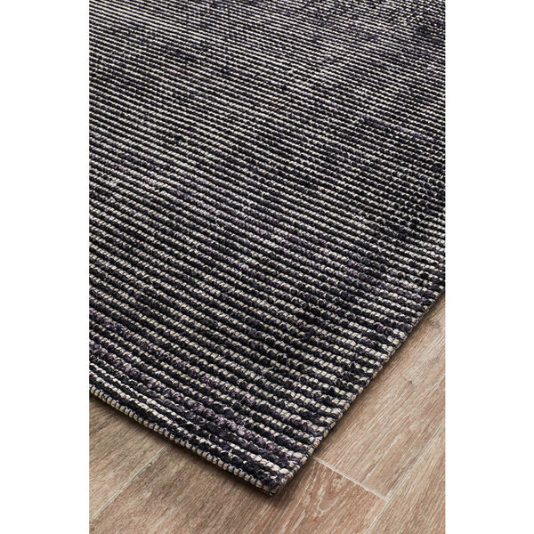 Black modern cut loop pile rug with subtle textured stripes on wooden floor.