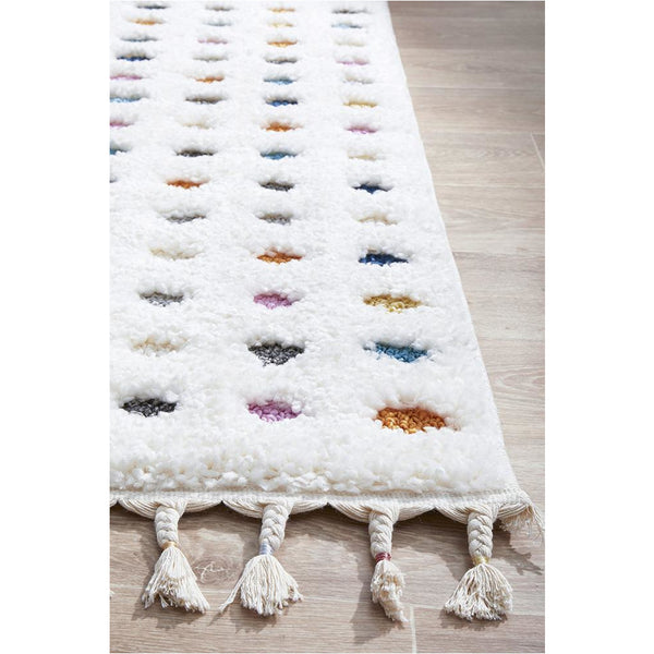 White shaggy rug with rows of colorful polka dots and tassels on one edge.