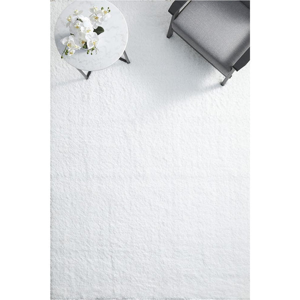 White rectangular shaggy rug with plush polyester pile under modern gray chair and round side table with white flowers.