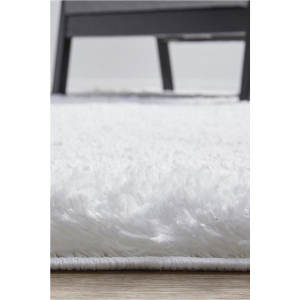 Close-up of a soft white shaggy rug with dense polyester pile and 5mm thickness next to dark wooden chair legs.