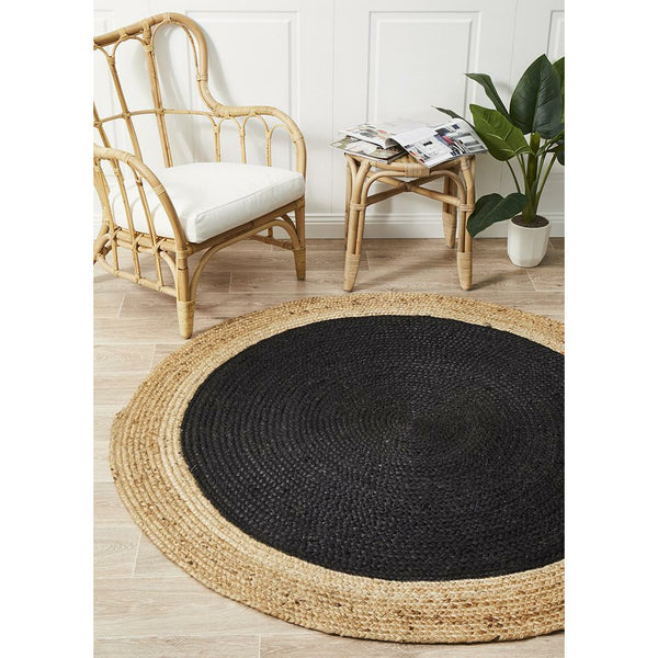 Round hand-woven black and natural jute rug with flatweave texture on light wood floor.