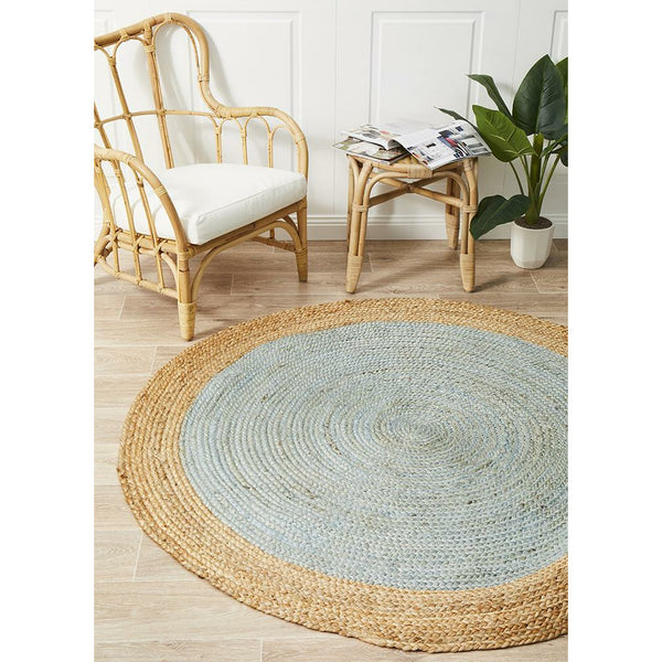 Round hand-woven natural jute rug with blue center and natural border on wooden floor.