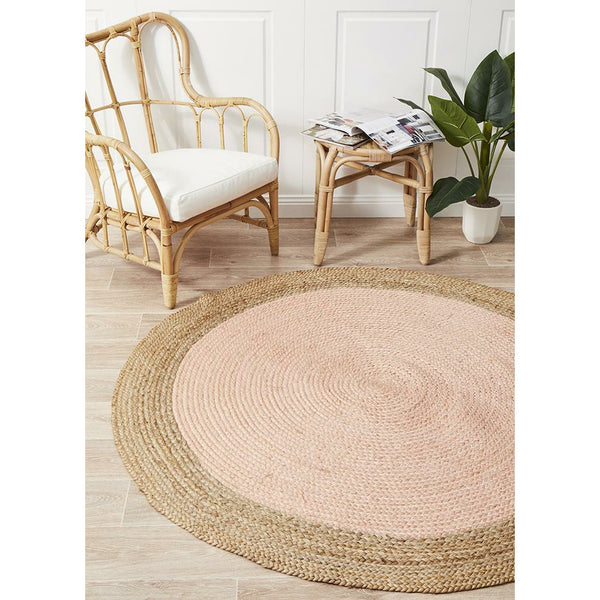 Round hand-woven natural jute rug with pink center and natural fiber border on wooden floor.