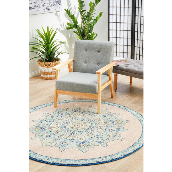 Round pastel rose blue multi-color transitional rug with intricate floral pattern under light gray wooden armchair.