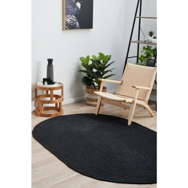 Black hand-braided oval jute rug with textured pile on light wood floor.