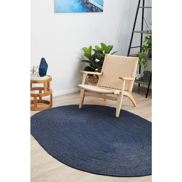 Oval navy blue jute rug with hand-braided textured design on light wood floor.