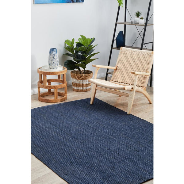 Rectangular navy blue hand-braided jute rug with textured pile in a bright, modern living room setting.