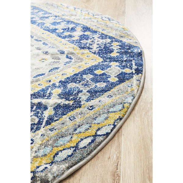 Round navy blue and yellow bohemian patterned rug on light wood floor.