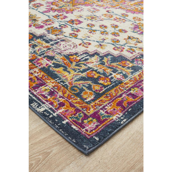 Rust pink beige bohemian rug corner with floral medallion pattern in multi-color on wood floor.