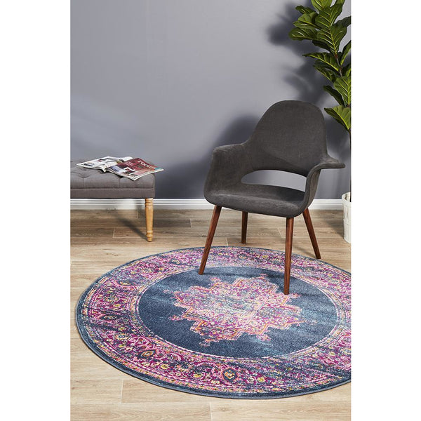 Navy blue round rug with pink and purple intricate bohemian pattern on hardwood floor beneath gray modern chair.