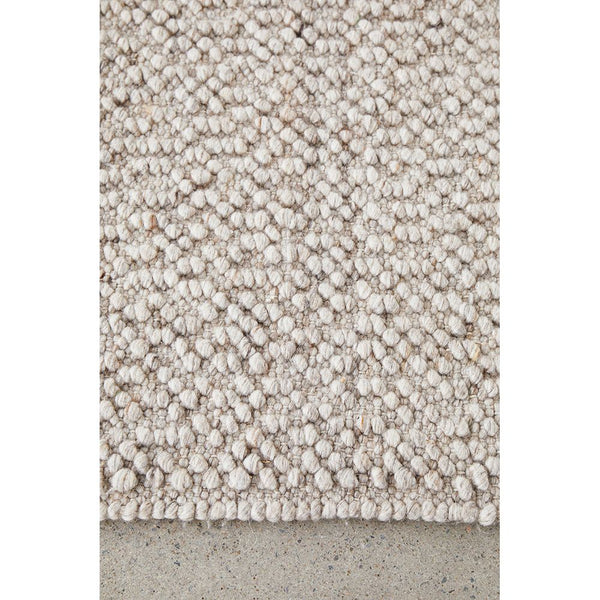 Natural wool blend rug with textured, looped pattern in soft neutral tones on concrete floor.