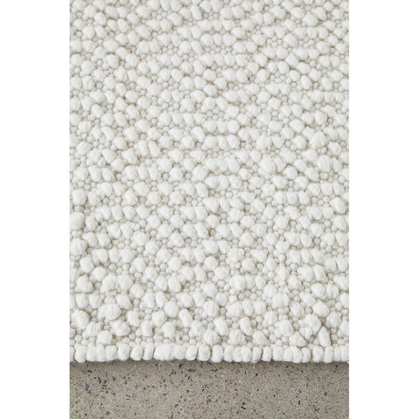 White boucle wool and polyester cotton rug with thick textured loops and a soft pile edge on concrete floor.