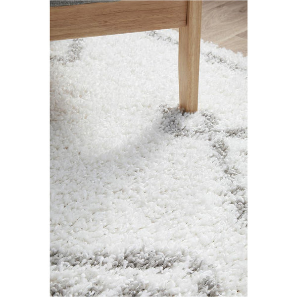 White shaggy rug with subtle gray tribal patterns and plush polypropylene pile beneath wooden furniture leg.