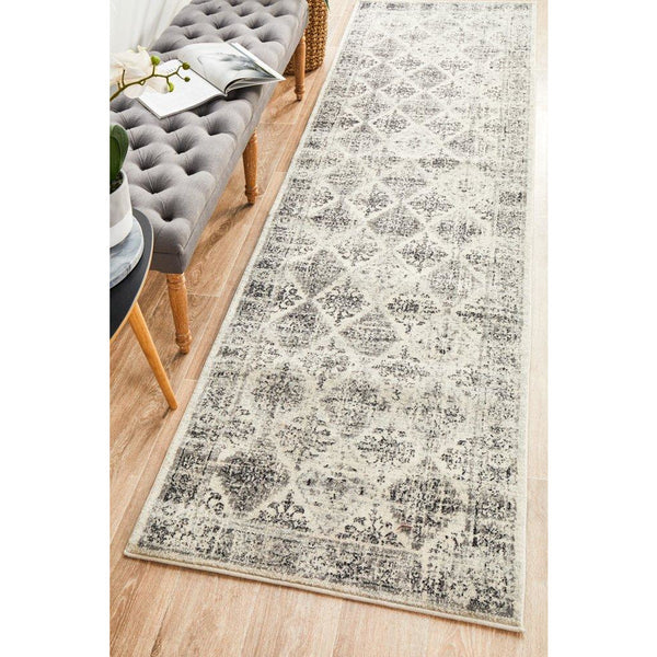Grey multi-color diamond patterned transitional runner rug on wooden floor by tufted grey bench.