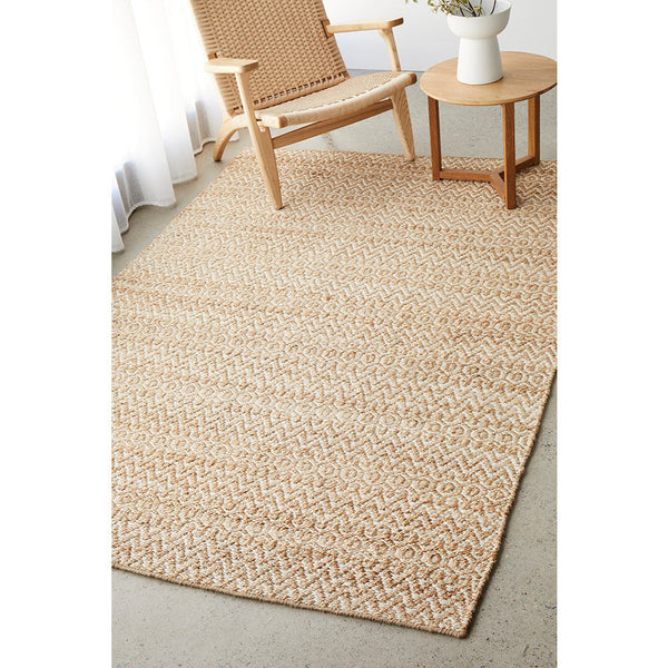 Natural woven jute and cotton rug with subtle zigzag pattern laid under wooden chair and round side table.
