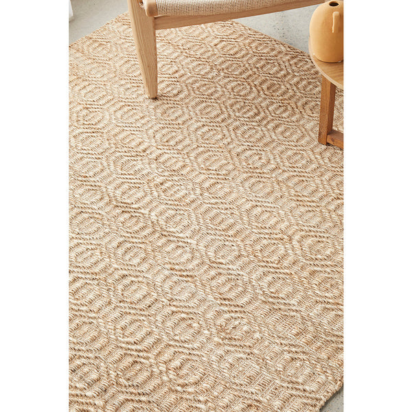 Natural jute cotton flatwoven rug with textured geometric pattern in beige tones under wooden chair and ceramic vase.