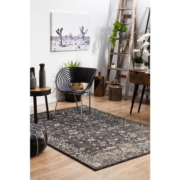 Charcoal and grey patterned transitional rug on light wood floor with modern black chair and decorative plants.
