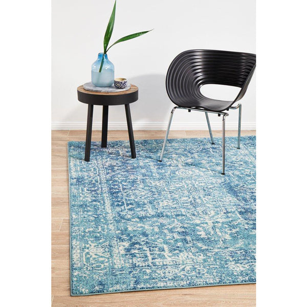 Blue transitional patterned rug with distressed design on wooden floor under black modern chair and small round table with.