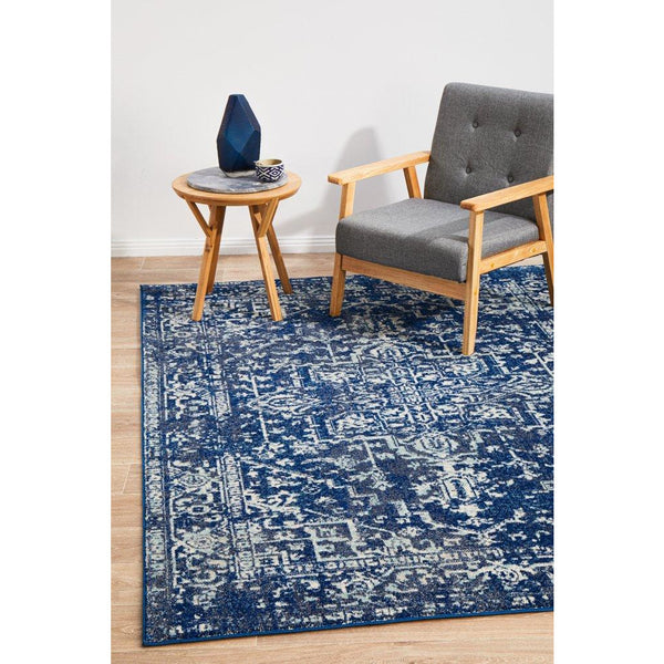 Navy blue patterned transitional rug with distressed design under gray armchair and wooden side table.