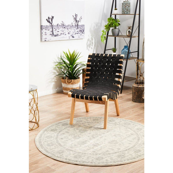 Round beige and light grey patterned rug under black woven chair on light wood floor.