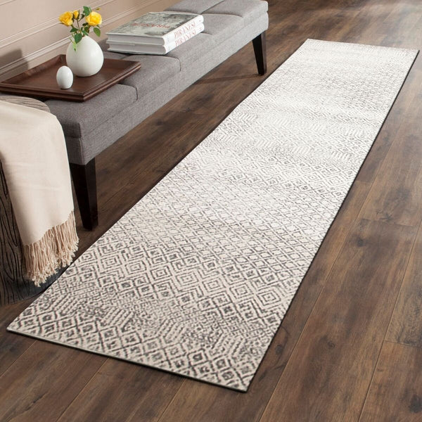 Grey beige patterned transitional runner rug on dark hardwood floor beside grey bench with books and vase.