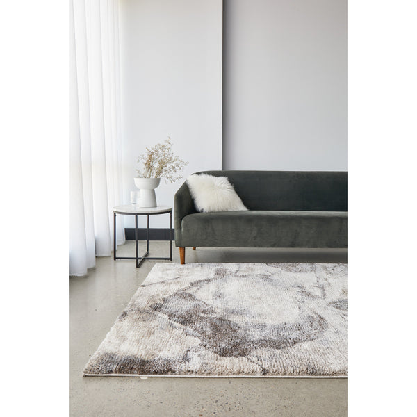 Multicolored abstract shag rug in neutral tones with high-pile texture beneath dark gray velvet sofa.