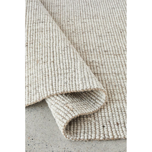 Beige wool jute rug with textured, hand-loomed pattern and natural fibers on concrete floor.