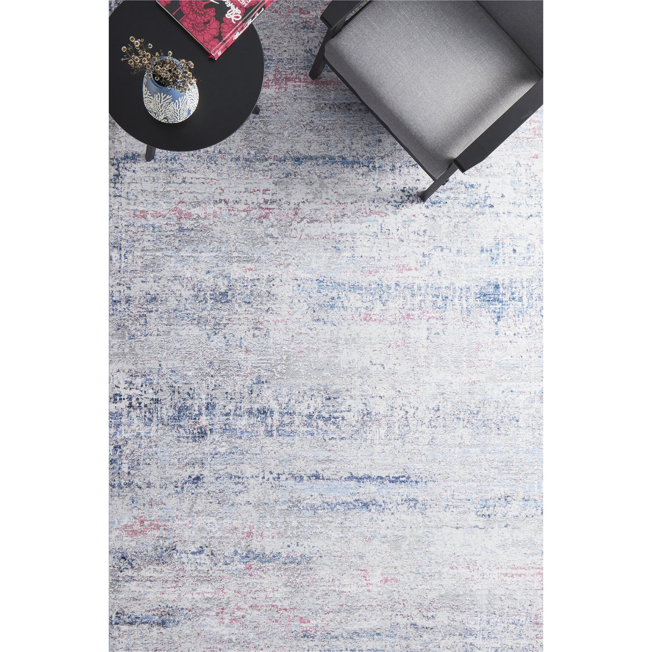 Transitional rug in blue and pink hues with a subtle abstract pattern under a gray armchair and black round table.