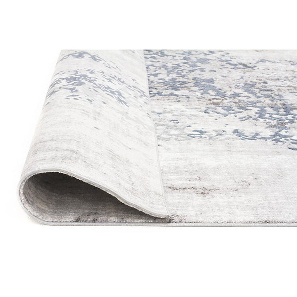 Grey, blue, and beige abstract patterned modern rug with soft, plush texture, rolled edge visible.