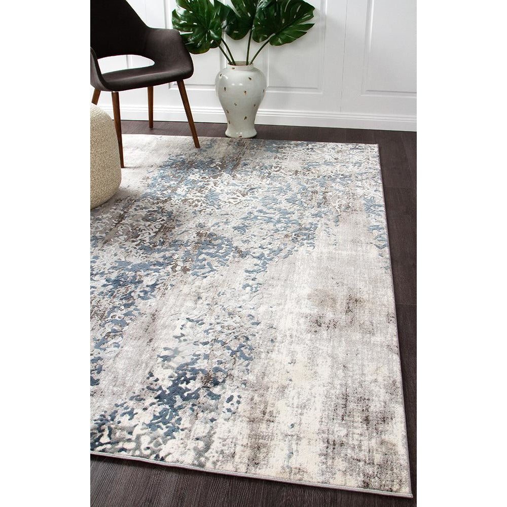 Modern rug with an abstract grey, blue, and beige pattern on a dark wood floor.