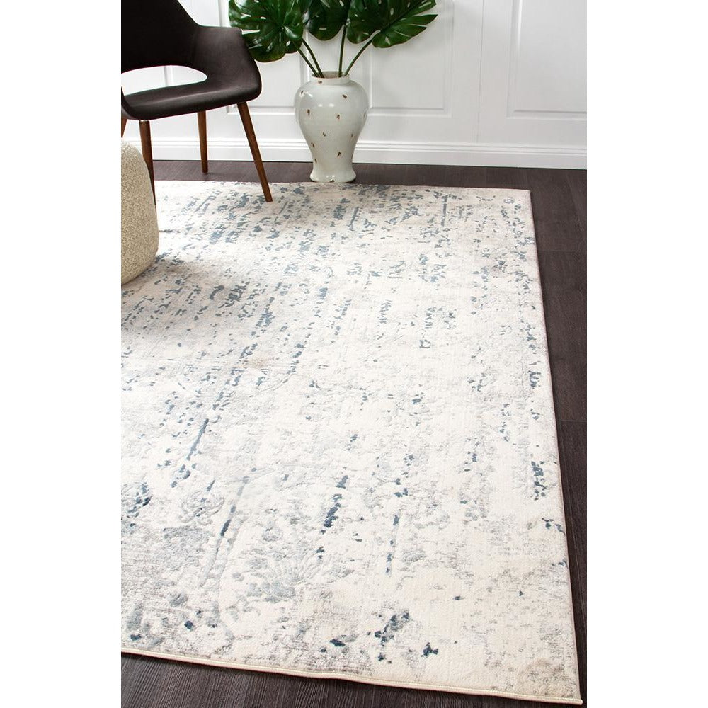 White rug with blue and grey abstract pattern, soft texture, modern style on dark wood floor.