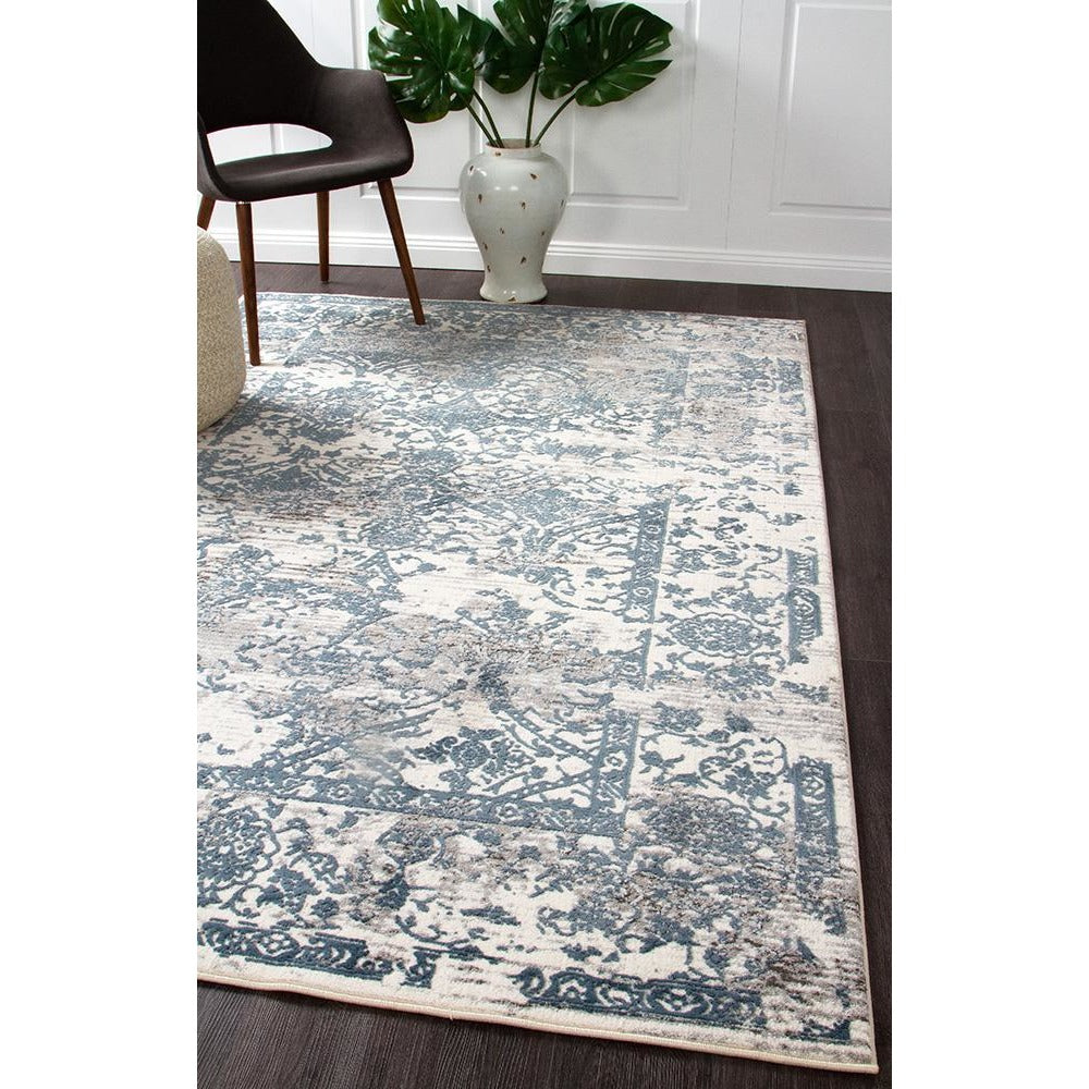 Modern rectangular rug with white, blue, and grey abstract floral border pattern on dark hardwood floor.