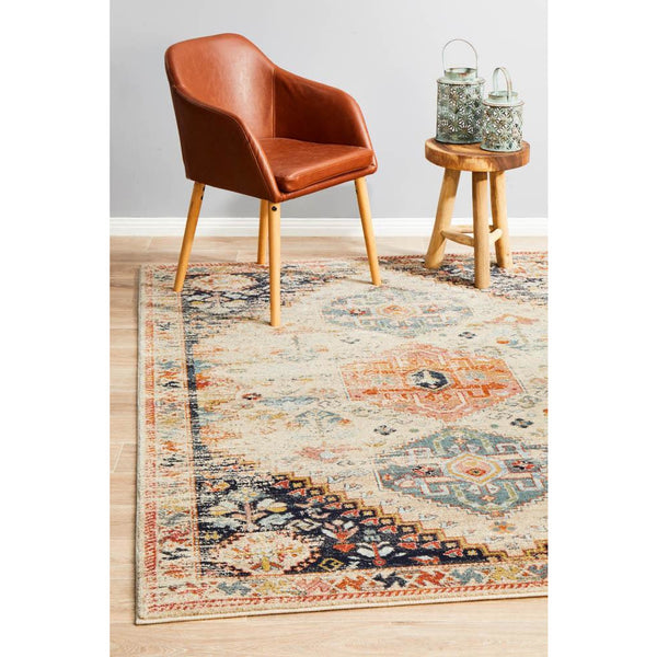 Multi-color transitional rug with autumn tones and tribal-inspired patterns under tan leather chair and wooden stool.