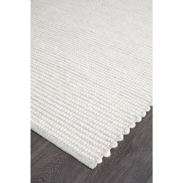 Light grey flat-woven wool rug with a subtle textured pile and scalloped edge on dark wood floor.
