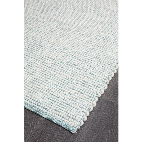 Turquoise blue flat-woven wool rug with textured chunky-knit border on dark floor.